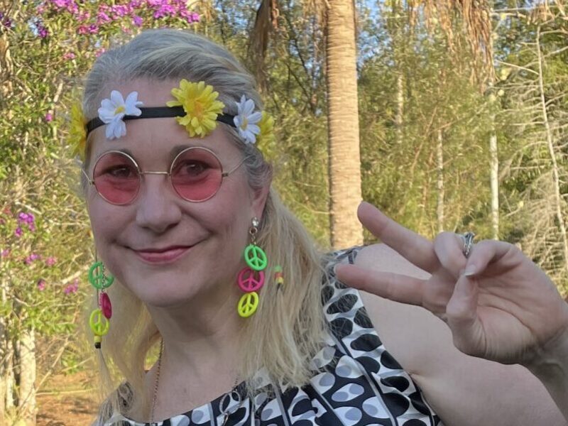 Sam dressed in fancy dress as a hippy, giving a peace sign.