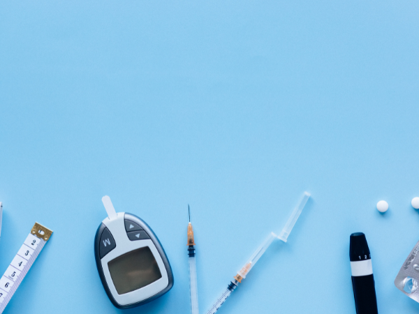 A glucometer, needles and lancet on a blue table.